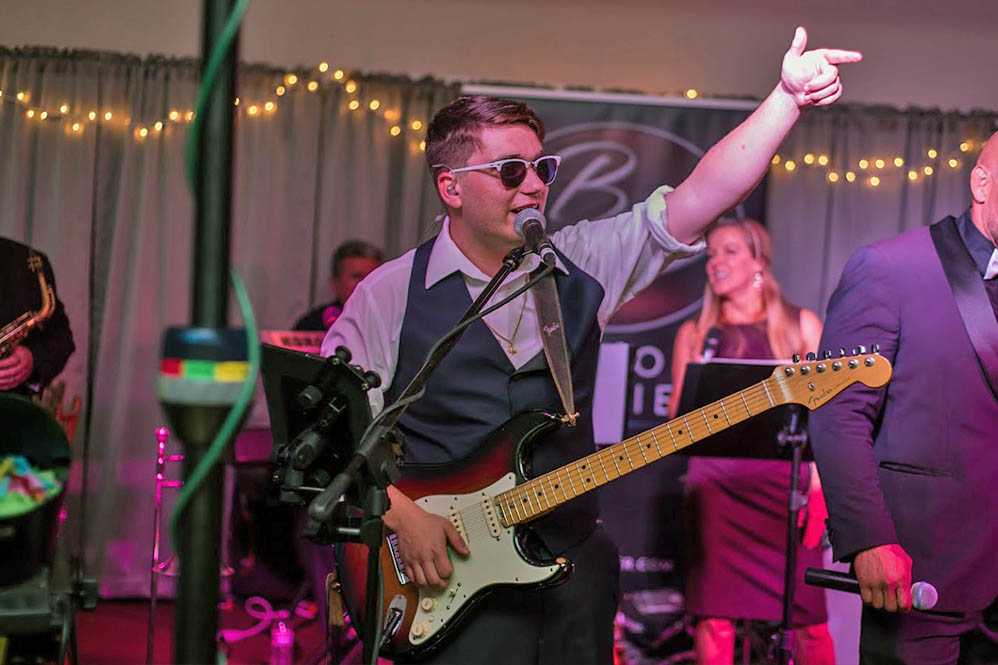The wedding band's guitar player raises his hand as he sings to the crowd.