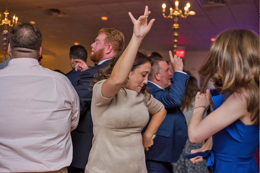 A wedding guest dancing with he hand raised as she enjoys the music of the Boston Wedding Band