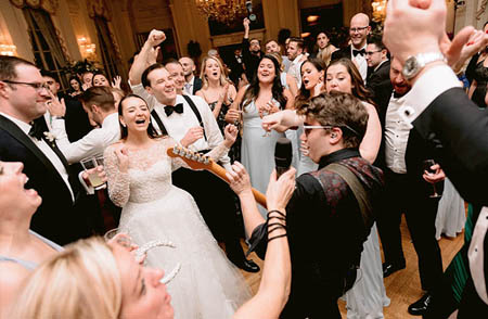 A bride and groom cheer in delight of the band's guitarist playing a solo.